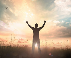 Image of a man with upraised arms facing sunrise