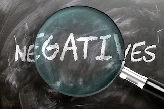 Image of a poorly cleaned blackboard with the word NEGATIVES written on it and a magnifying glass centered on the letters GATI